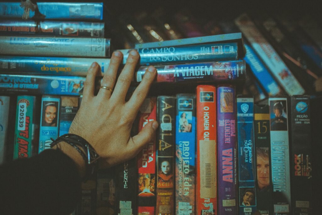 A hand reaching for a classic VHS tape from a colorful vintage collection indoors.